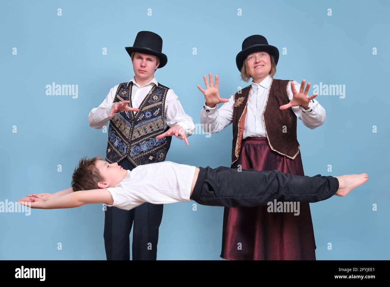 Magicians levitated a boy in the air, circus performers on a blue background Stock Photo