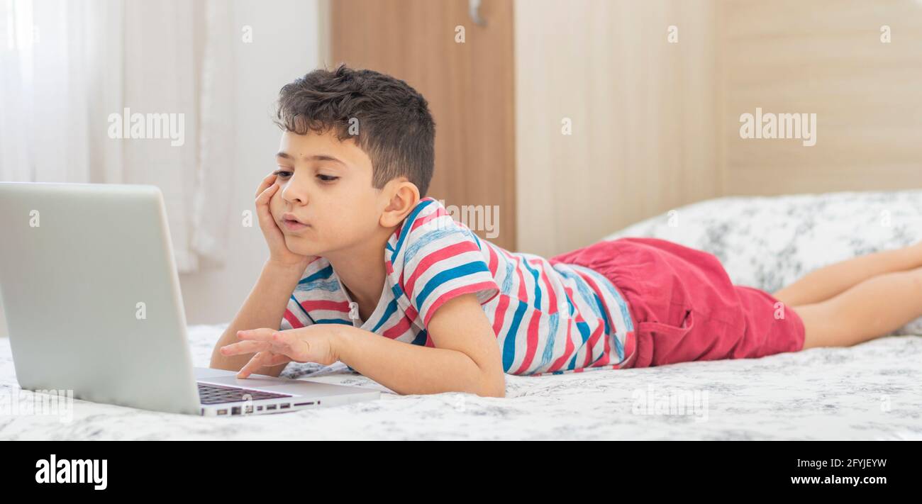 Young Boy Child Lying On Bed Using A Laptop Online Class Lesson On young-boy-child-lying-on-bed-using-a-laptop-online-class-lesson-on