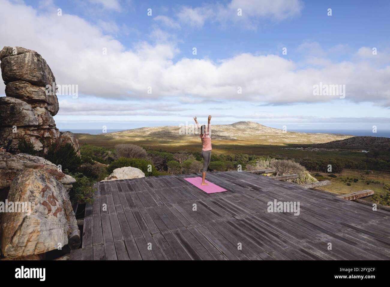 Caucasian woman practicing yoga standing on one leg stretching in rural mountain setting Stock Photo
