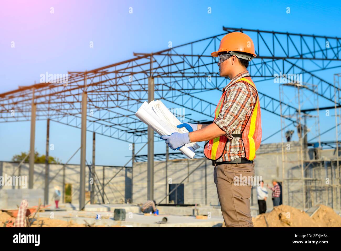 Engineer standing on a building site looking at building blueprint, Thailand Stock Photo
