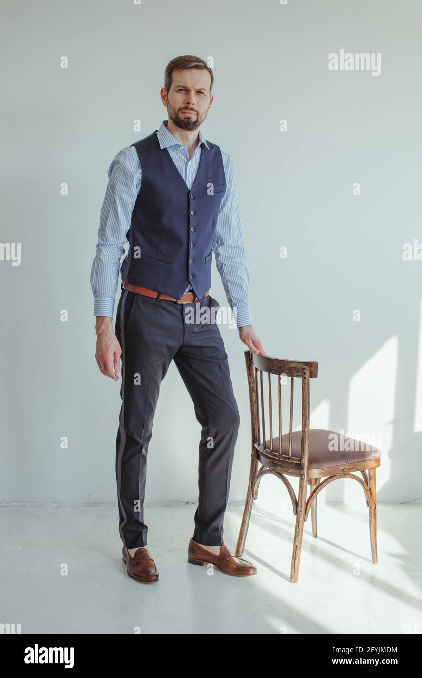 Portrait of a man in a shirt and waistcoat standing next to a chair in sunlight Stock Photo