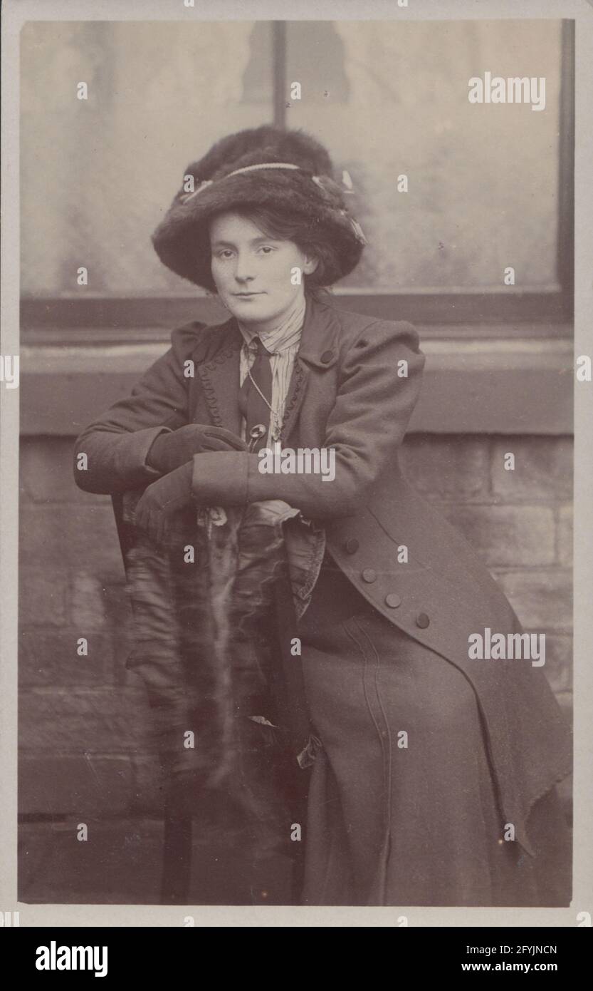 Vintage early 20th century photographic postcard Showing a fashionable young lady sat on a chair outside a house. Stock Photo