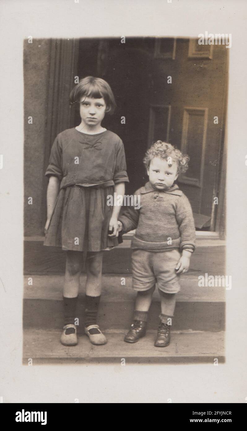 Vintage early 20th century British photographic postcard showing two poor, and sad looking children holding hands. Stock Photo