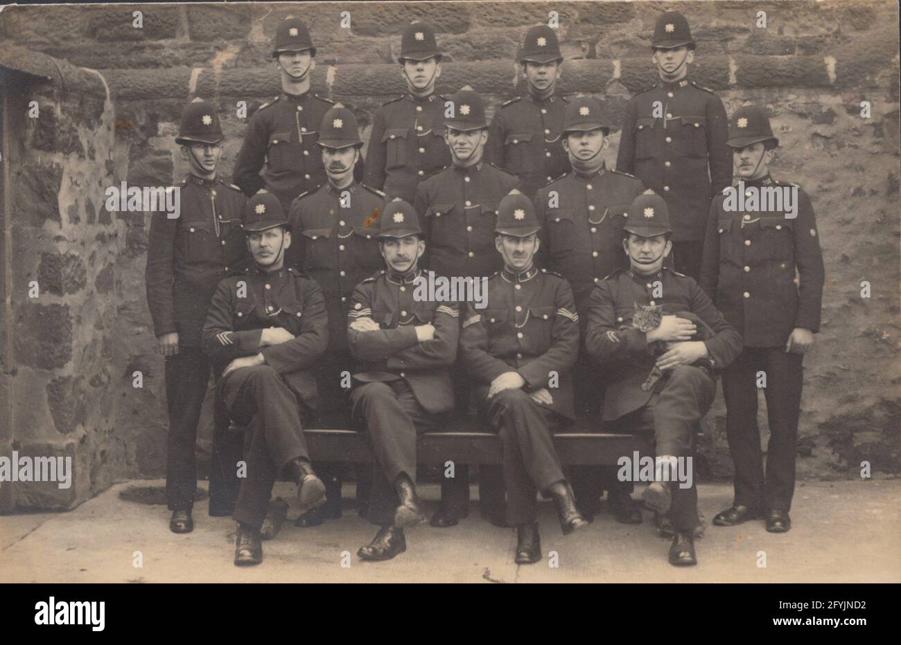 Vintage early 20th century photographic postcard showing a group of British Policemen. One of the Police Officers holding the station cat. Stock Photo