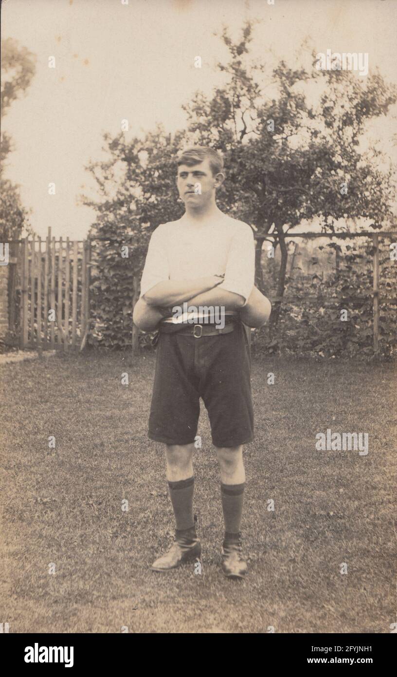 Vintage early 20th century photographic postcard showing a young man stood in a garden wearing shorts and boxing gloves. Stock Photo