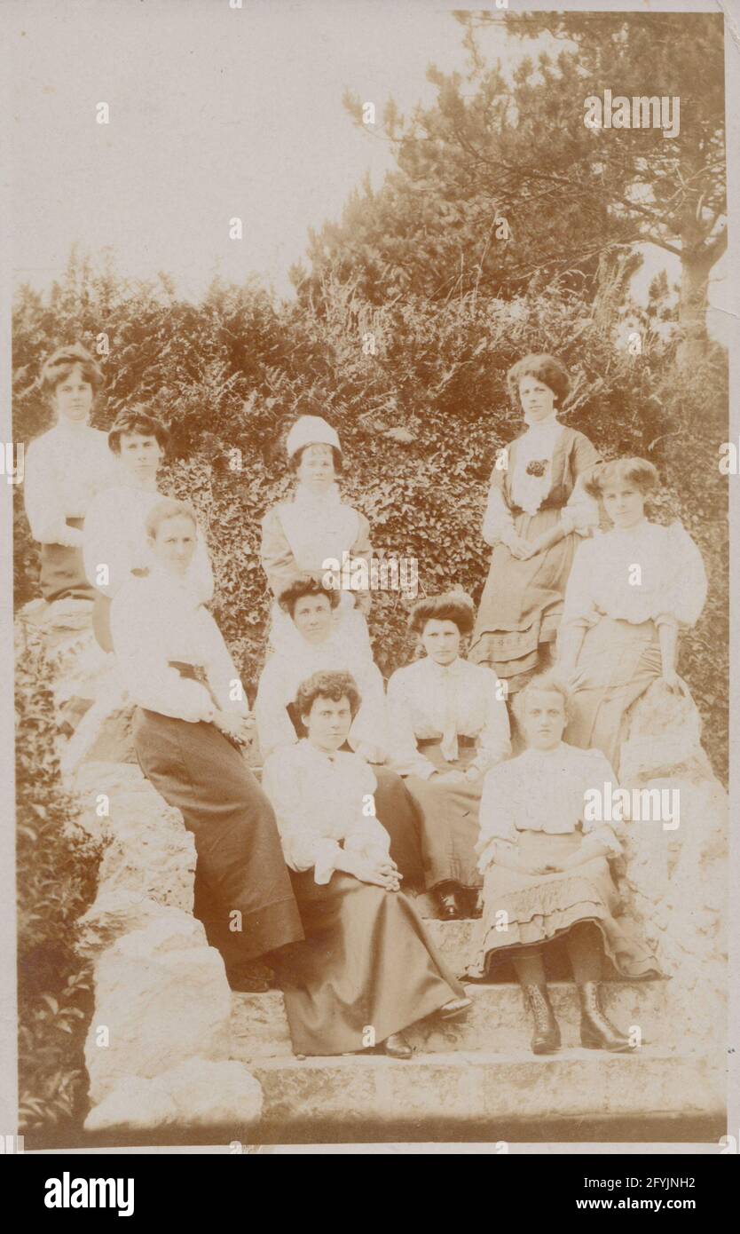 Vintage early 20th century photographic postcard showing a group of young ladies sat, and stood on some imposing steps. One of the ladies appears to be a nurse. Stock Photo