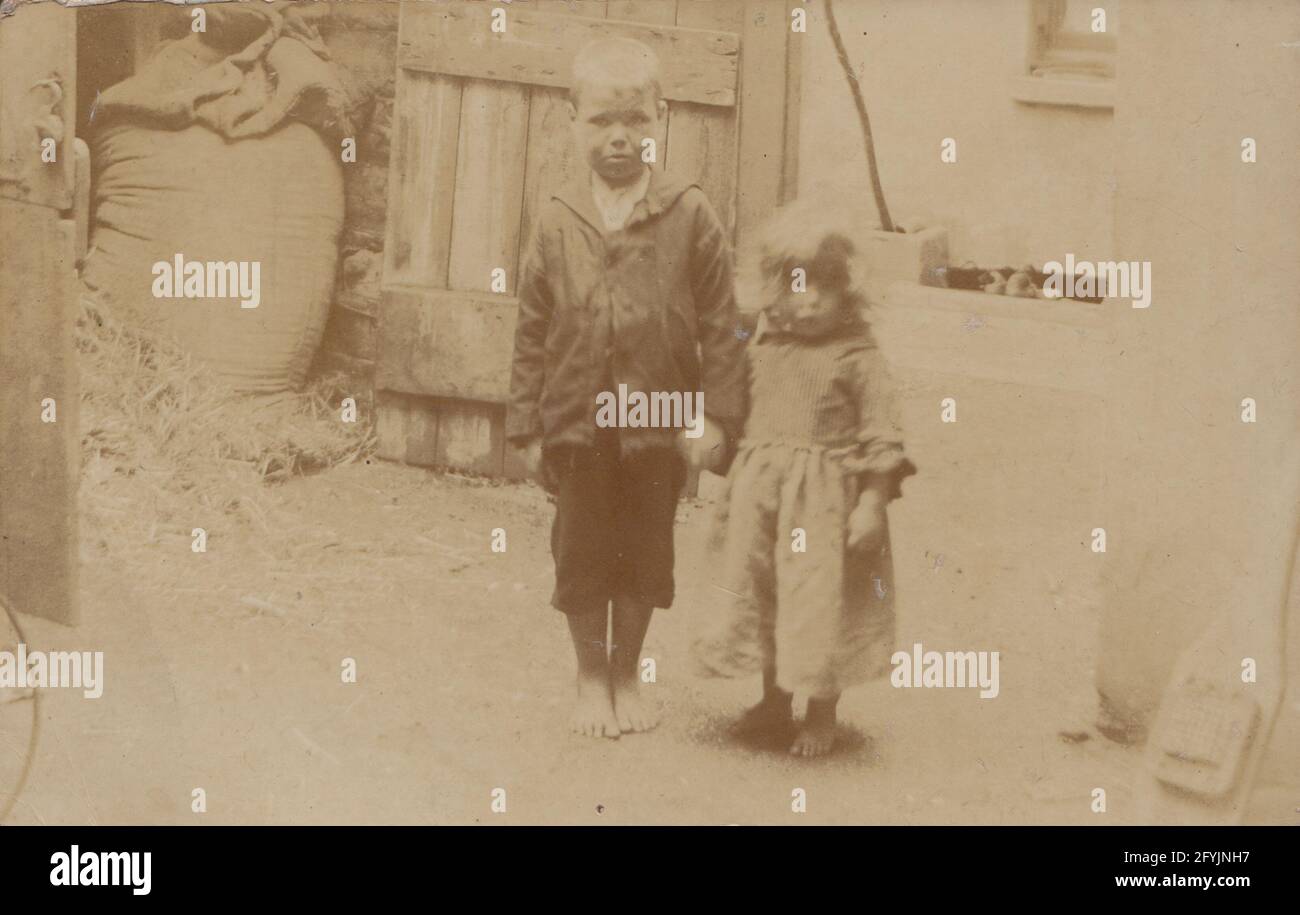 Vintage 1906 photographic postcard showing a destitute brother and sister holding hands. Wearing shabby clothes with no footwear. Stock Photo
