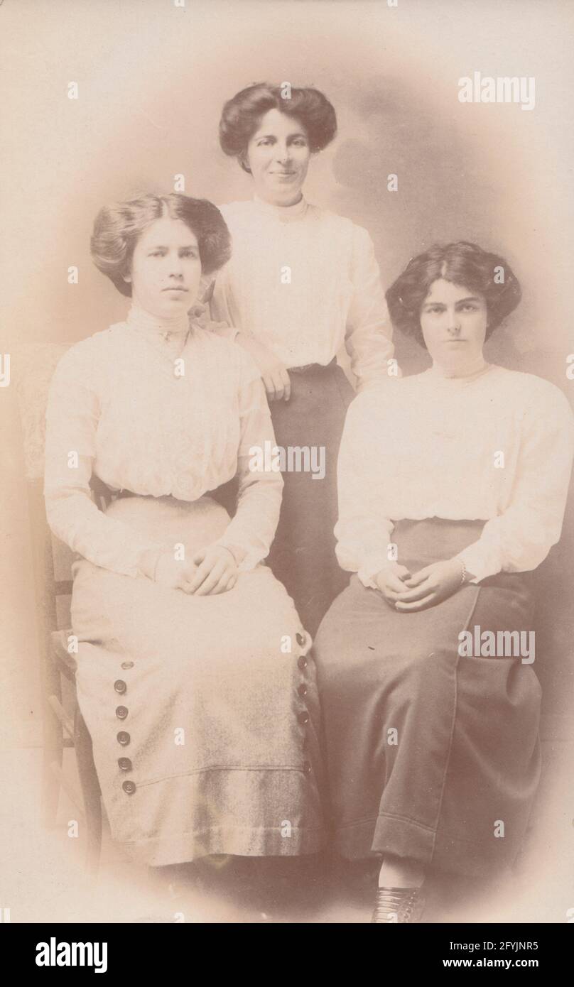 Vintage early 20th century photographic postcard showing a three ladies. Possibly a mother and her two daughters. All have similar hairstyles. Stock Photo