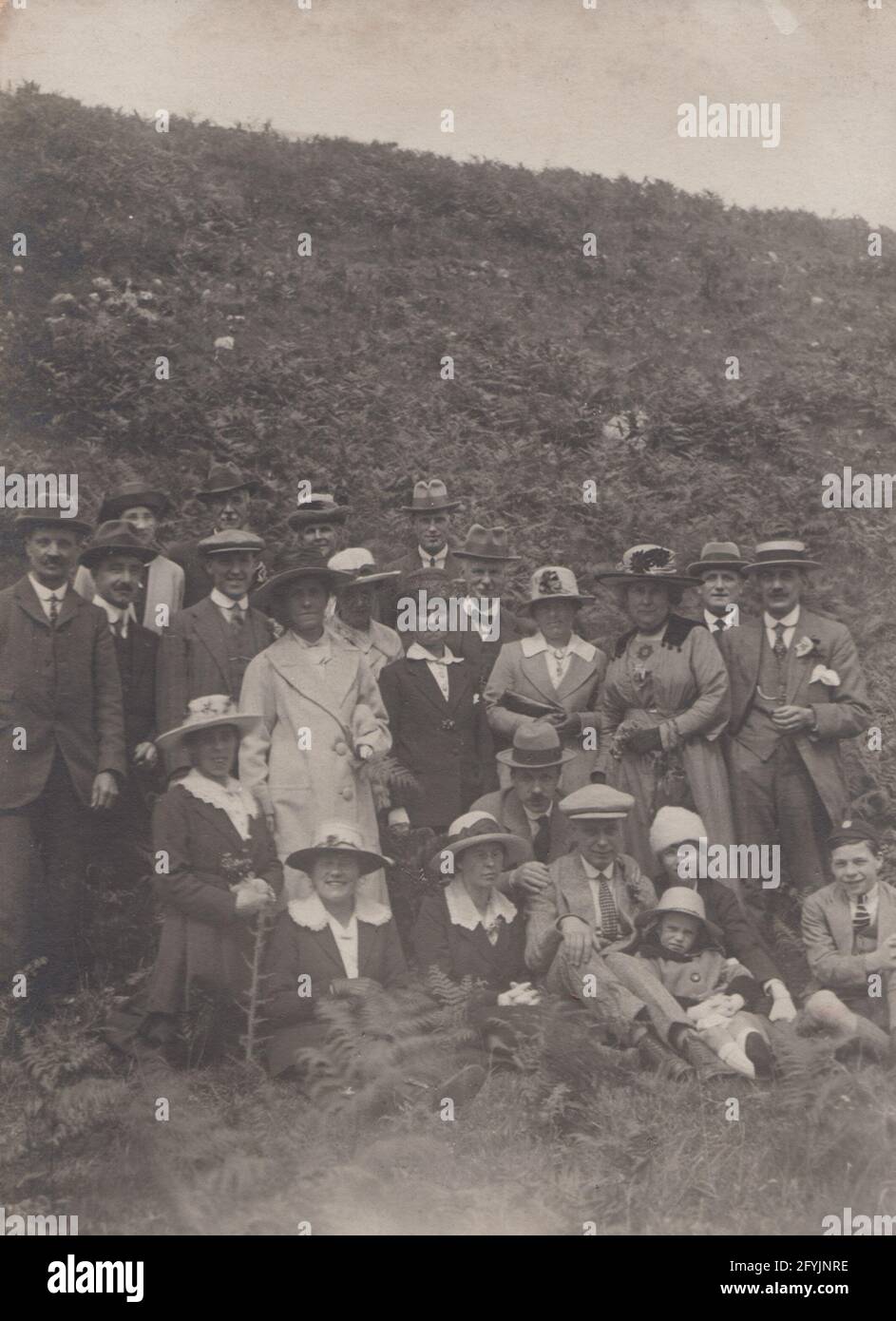 Vintage early 20th century photographic postcard showing a group of people on an outing to the coast or countryside. Stock Photo