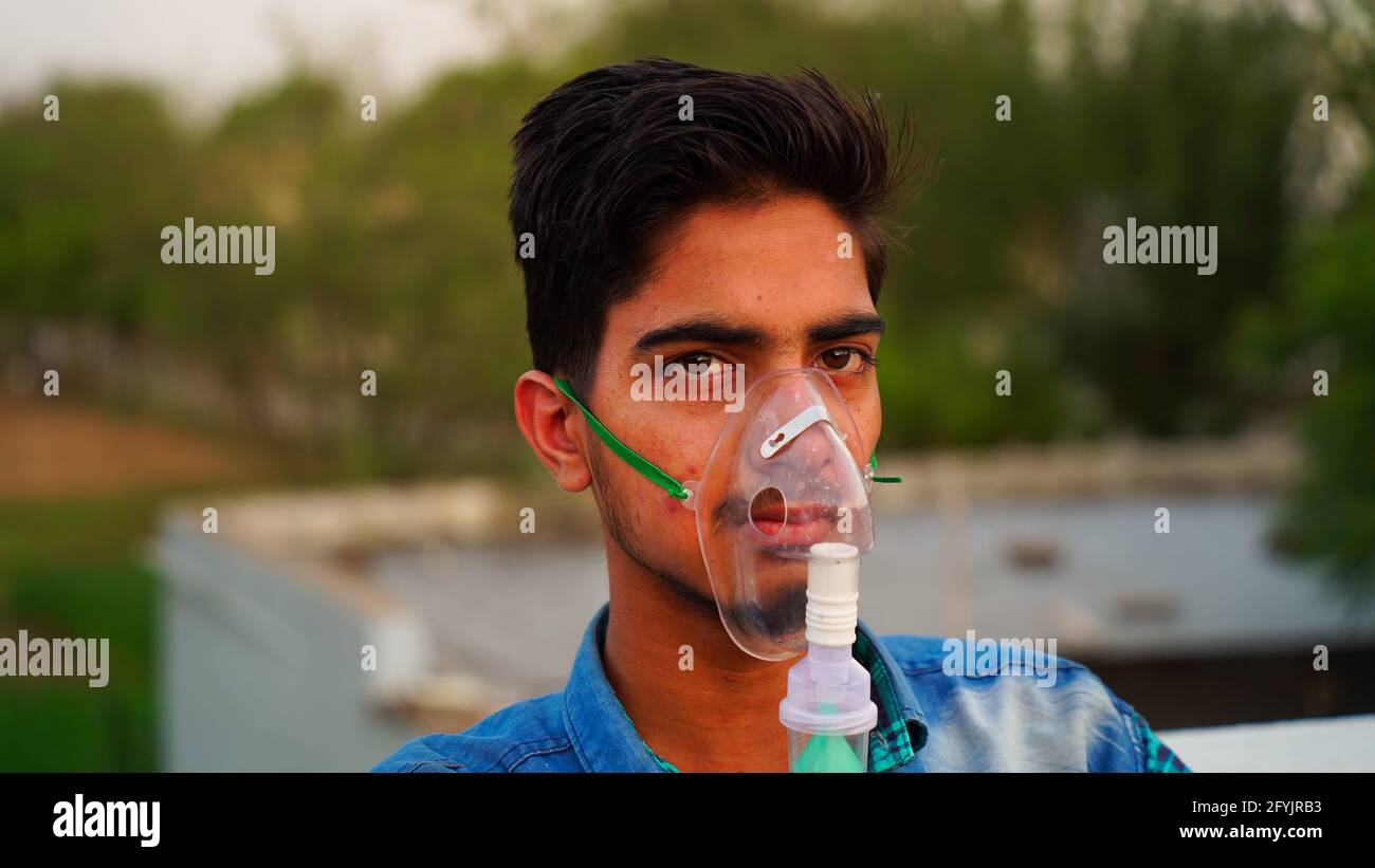 Man infected with Coronavirus disease. Indian patient inhaling oxygen wearing mask outside of hospitals. Adult boy breathing with nebulizer Surviving Stock Photo