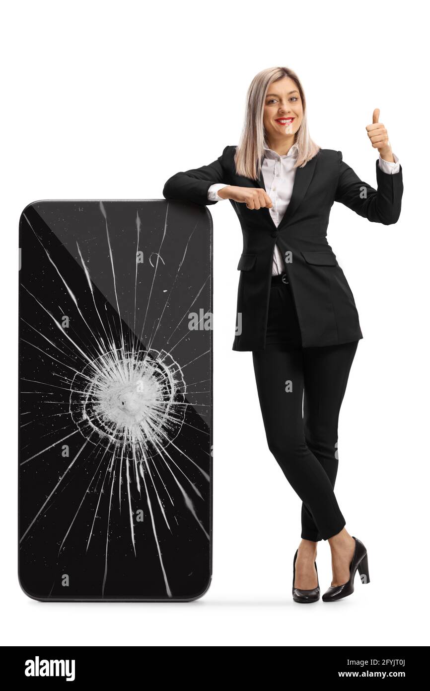 Full length portrait of a professional woman leaning on a smartphone with cracked screen and showing thumbs up isolated on white background Stock Photo