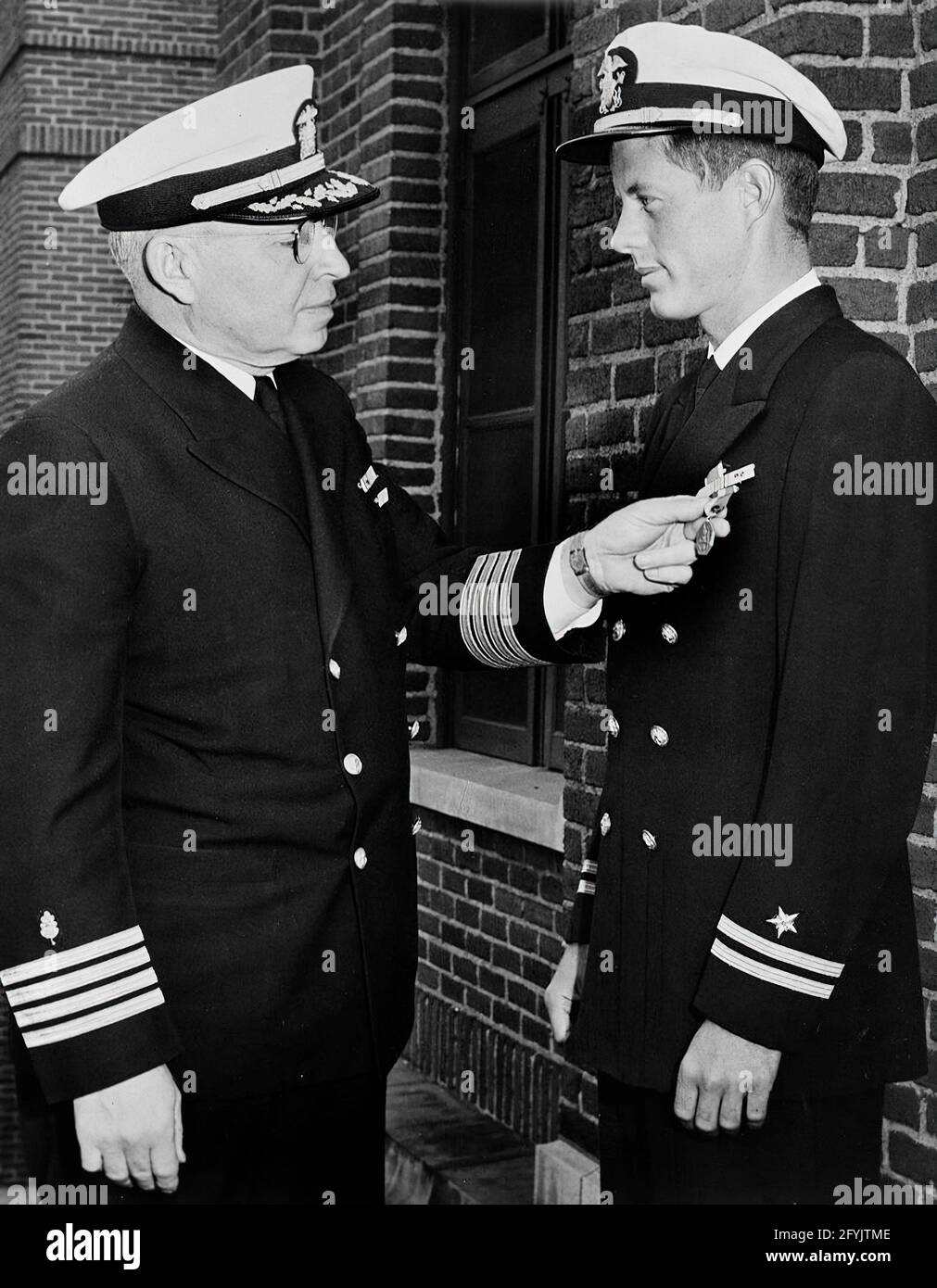 Lieutenant John F. Kennedy being awarded the Navy and Marine Corps Medal for heroism in rescuing members of the crew of the PT-109; original photograph taken 11 June 1944. Captain Frederick L. Conklin, Commandant of Chelsea Naval Hospital; John F. Kennedy. Chelsea Naval Hospital, Chelsea, Massachusetts. Stock Photo