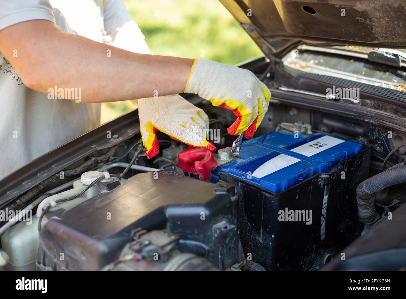 Man unscrews the battery mounting bolts with a wrench, installing and replacing spare parts on a car. Stock Photo