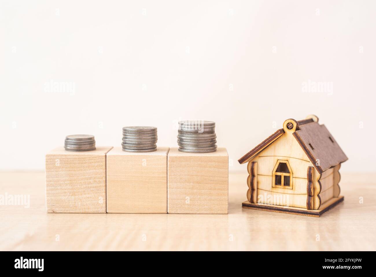 Model of house with stacks of coins on wooden blocks on beige table Stock Photo
