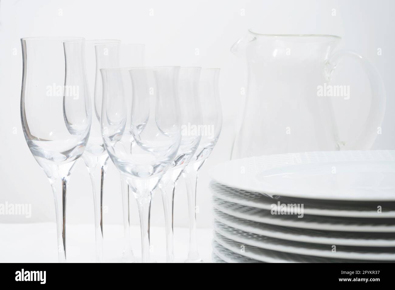 Set of stacked plates, crystal stemware and a glass jug on a white