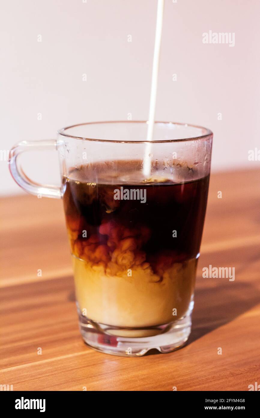 Milk poured in black coffee Stock Photo