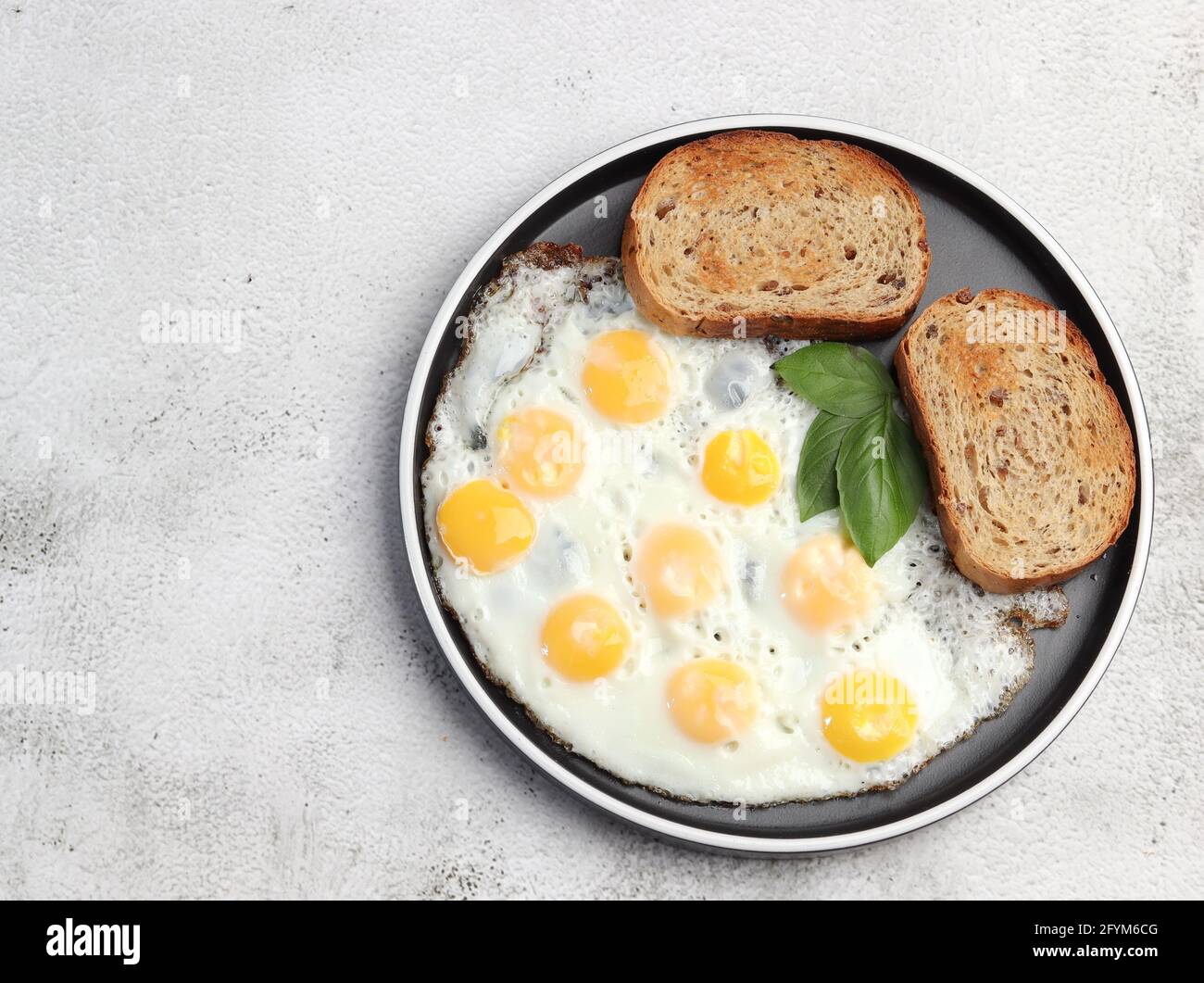 Fried quail eggs on a round plate on a light gray background. Top view, flat lay Stock Photo