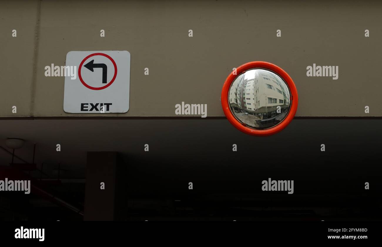 Closeup convex mirror mounted on cement wall near exit sign in parking
