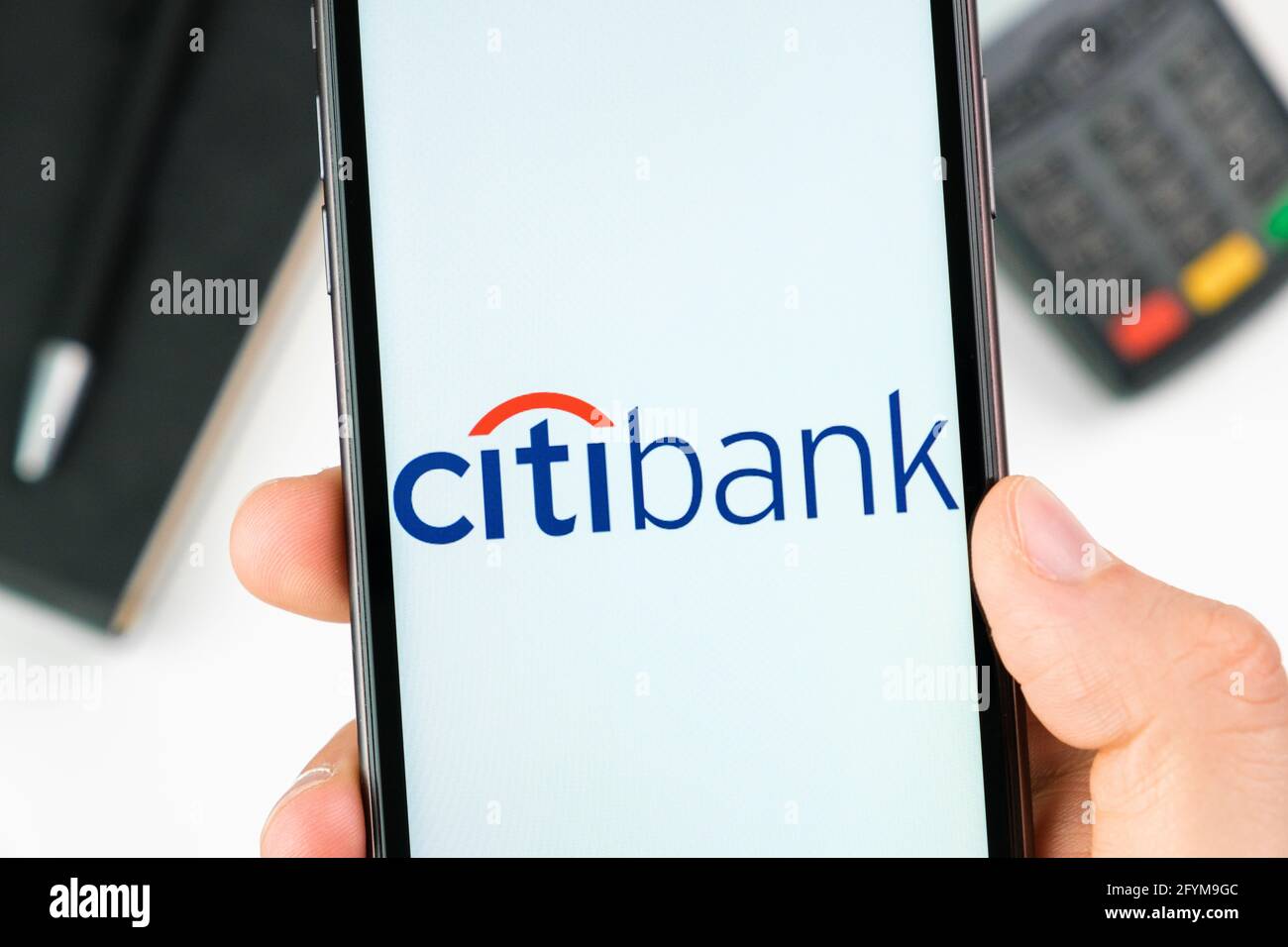 Citi bank logo on the smartphone screen in mans hand on the background of payment terminal, May 2021, San Francisco, USA Stock Photo