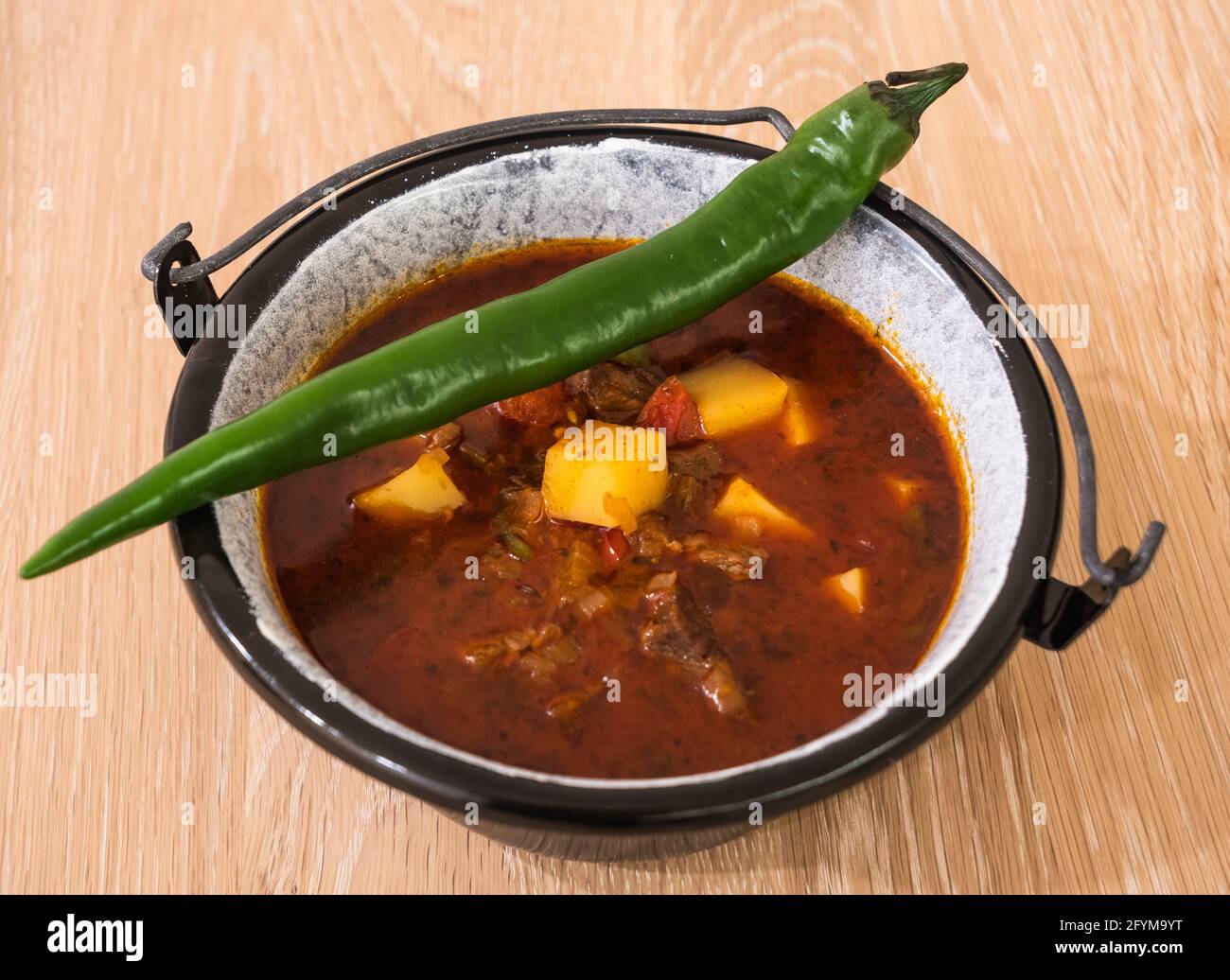 Hungarian Beef Goulash or Gulyas Soup or Stew Served in a Small Cauldron with Potatoes, Meat, Paprika and Green Chili Pepper Stock Photo