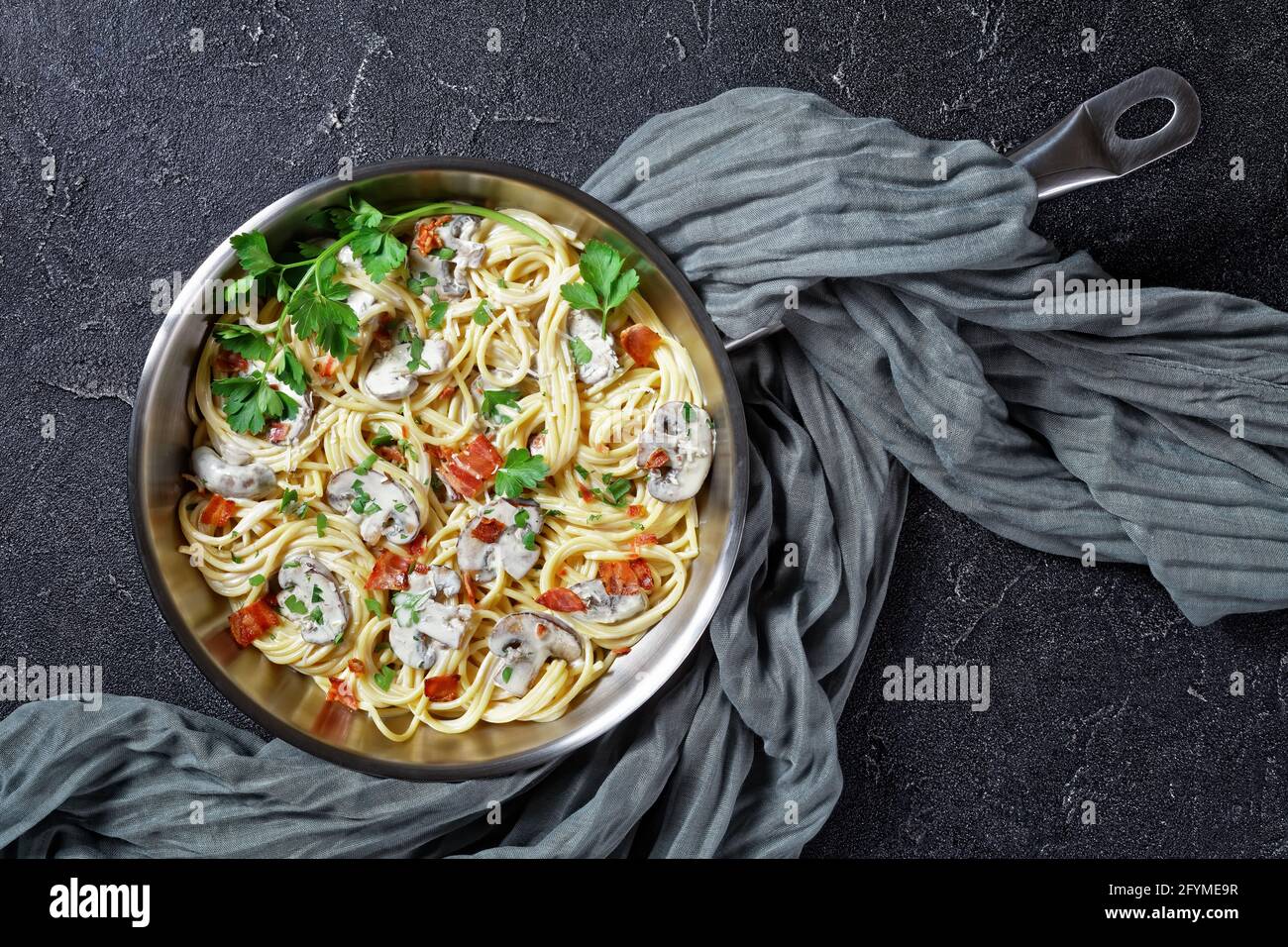 Italian pasta with cremini mushroom sauce of heavy cream and parmesan  cheese with crispy bacon and fresh parsley served on a metal skillet on a dark Stock Photo