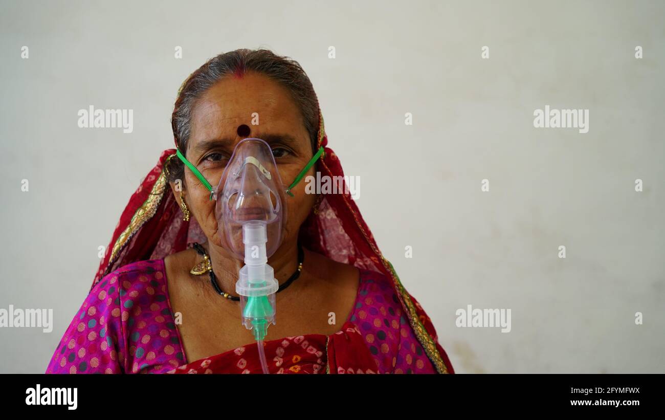 May 2021- Jaipur, India. Old Indian woman infected with Covid 19 disease. Patient inhaling oxygen wearing mask with liquid Oxygen flow. Stock Photo