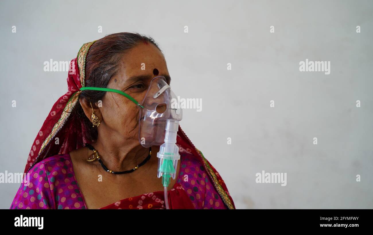 May 2021- Sikar, India. Old Indian woman infected with Covid 19 disease. Patient inhaling oxygen wearing mask with liquid Oxygen flow. Stock Photo