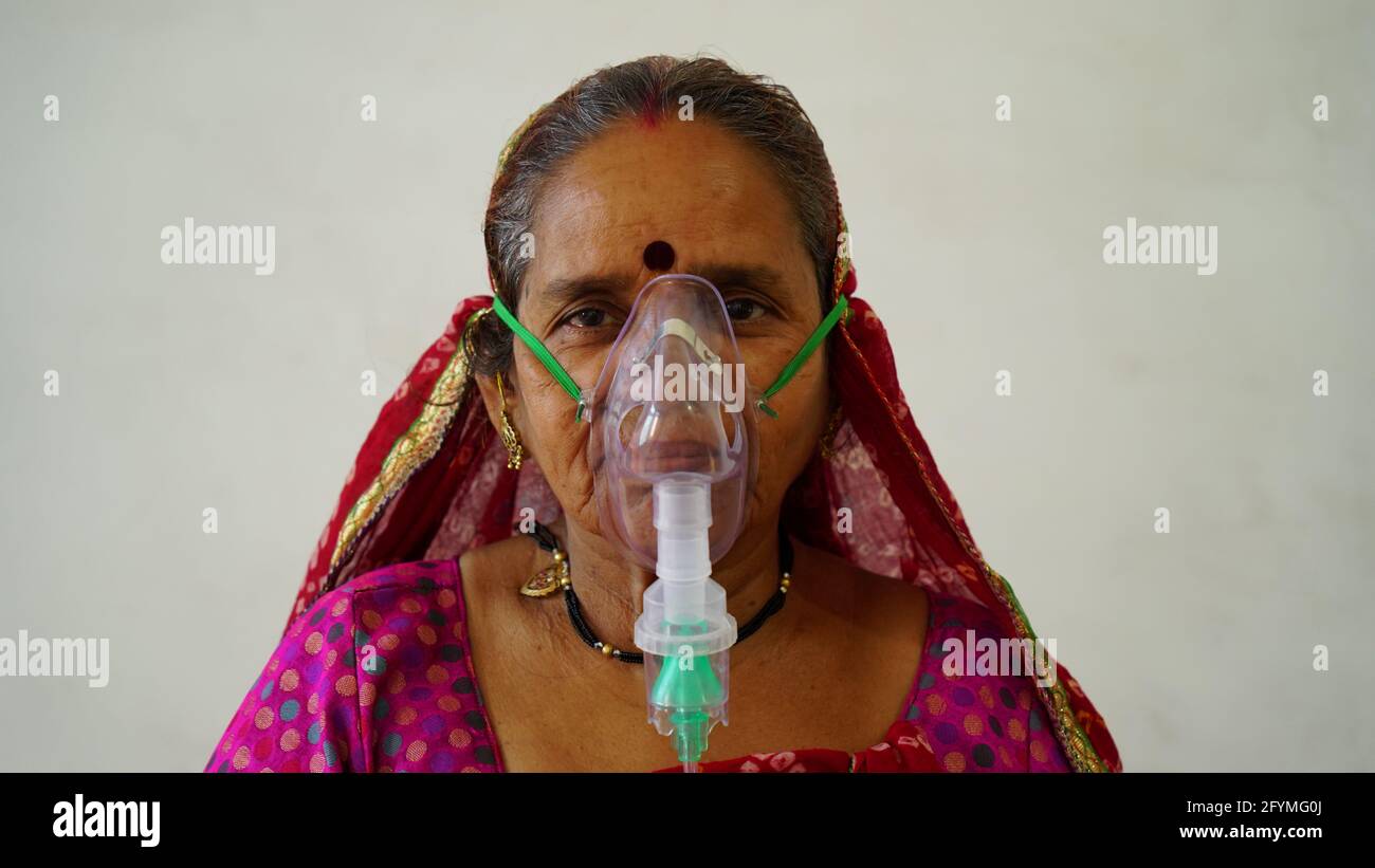 May 2021- Jaipur, India. Old Indian woman infected with Covid 19 disease. Patient inhaling oxygen wearing mask with liquid Oxygen flow. Stock Photo