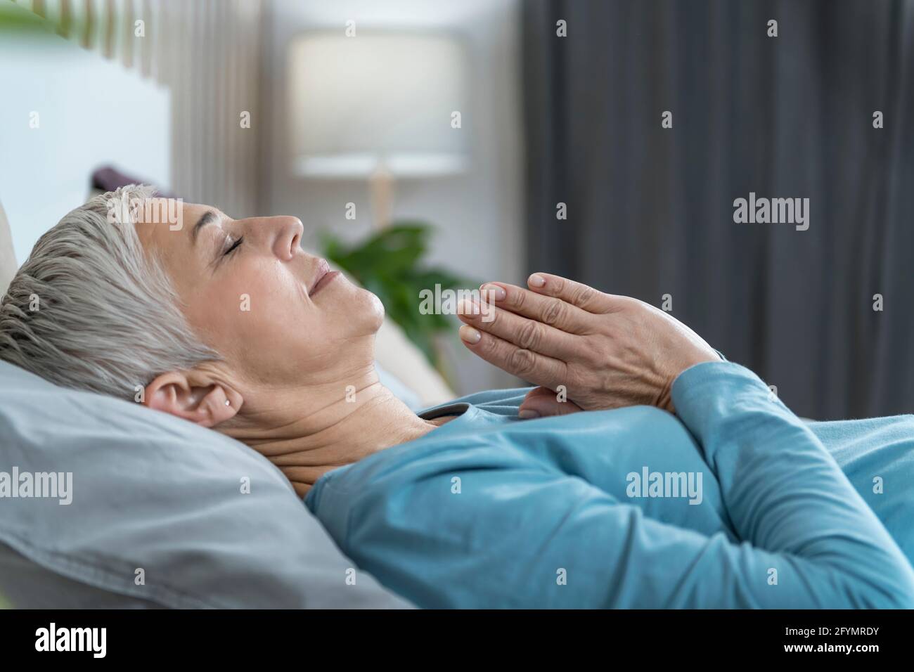 Woman lying in bed meditating Stock Photo