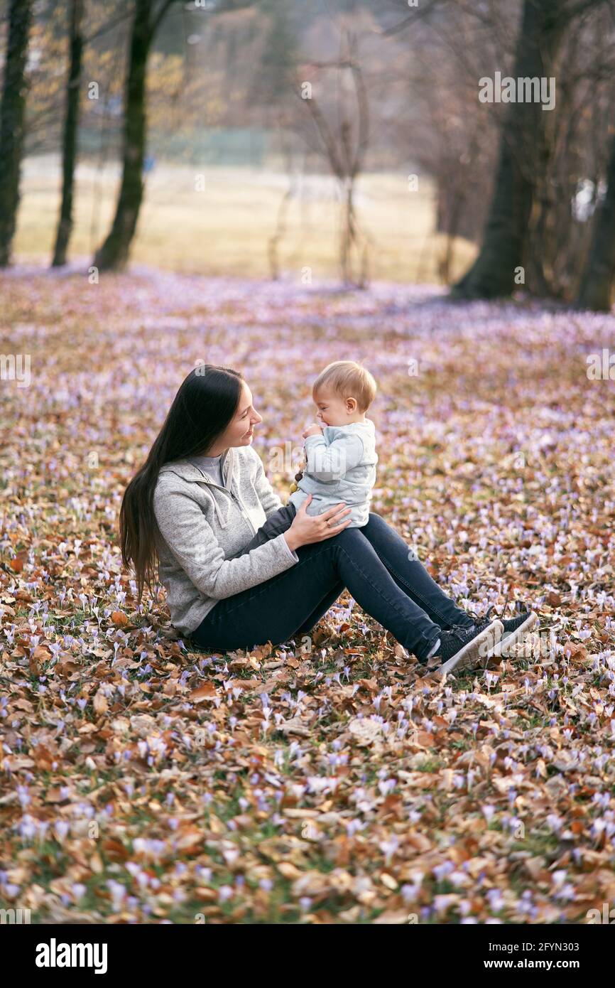 Mom sits on fallen leaves in the park, holding the baby on her lap, sitting  with him face to face Stock Photo - Alamy