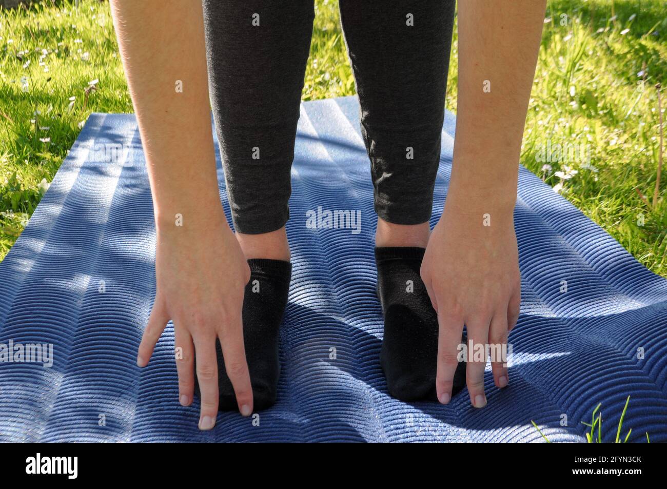 Woman wearing grey leggings and black socks, practicing yoga and stretching on a blue mat on the green grass outdoor Stock Photo