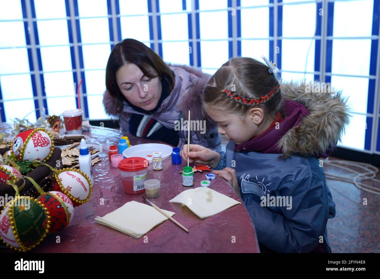Little girl painting picture on a Christmas ornament, adult watching ...