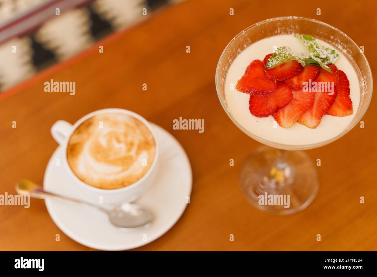 Creamy dessert with strawberries in glass, cappuccino on wooden table. Appetizing dessert and