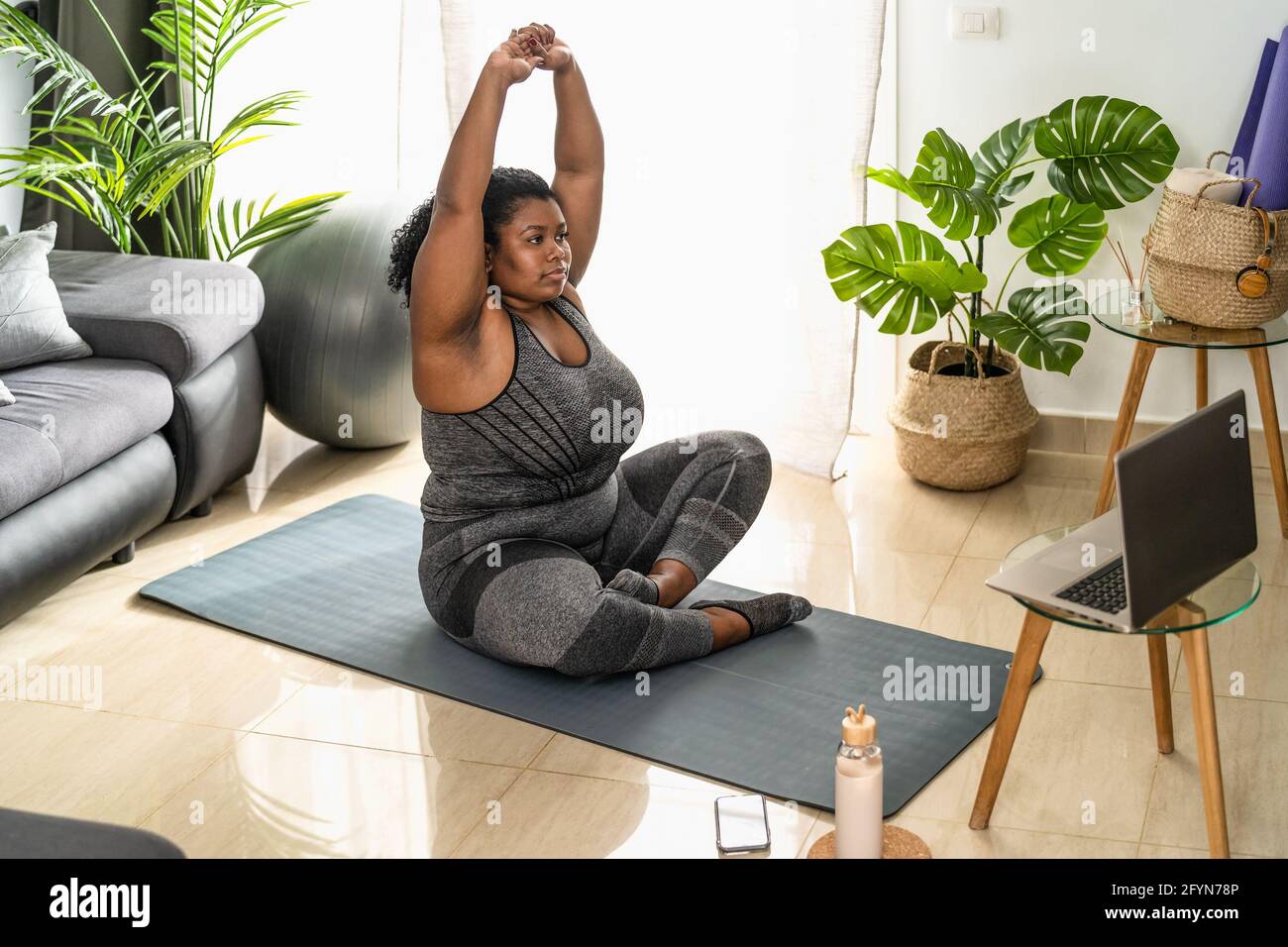 Young African curvy woman doing pilates online fitness class with
