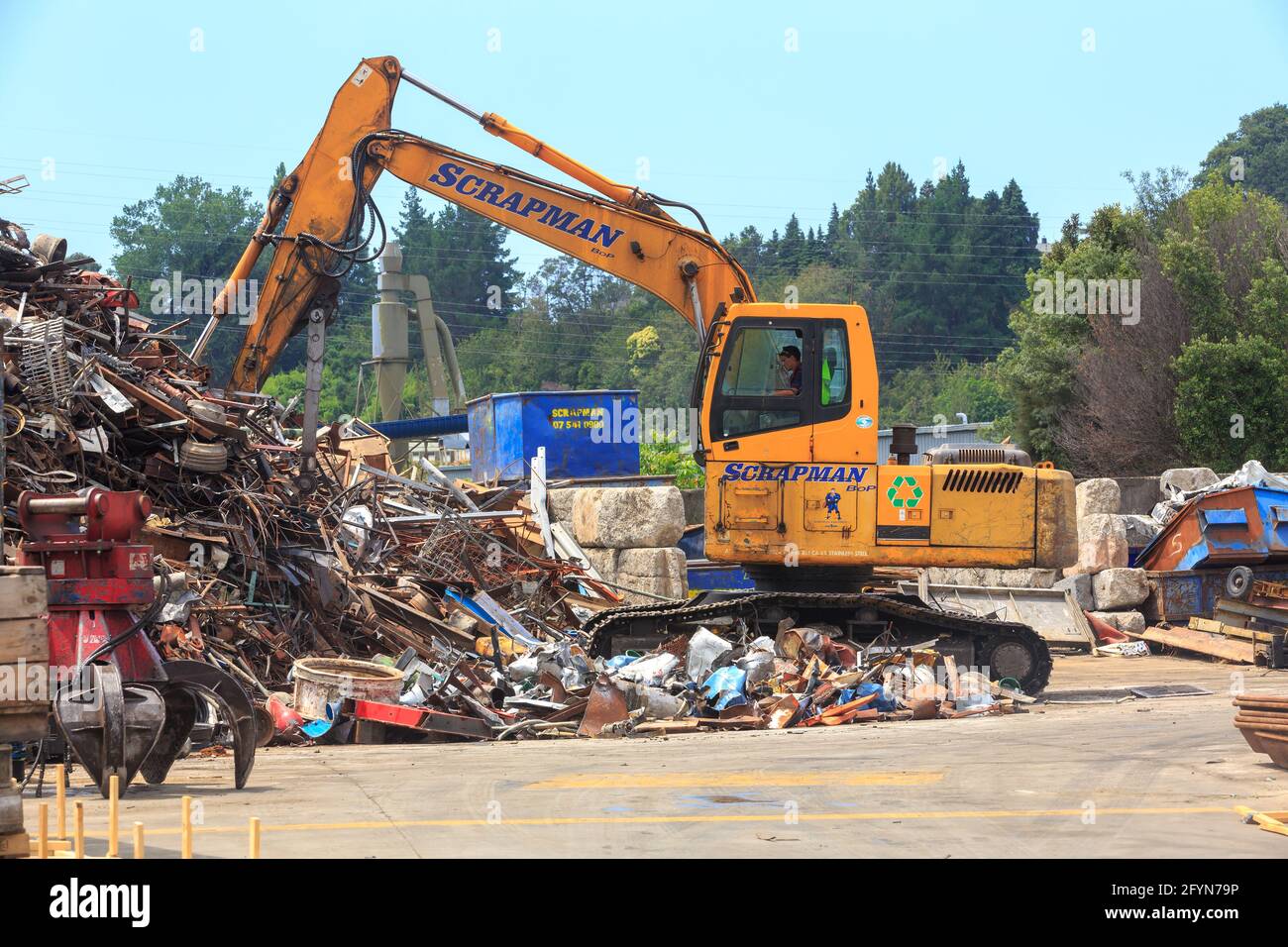 A man using an excavator to move a pile of scrap metal. Tauranga, New