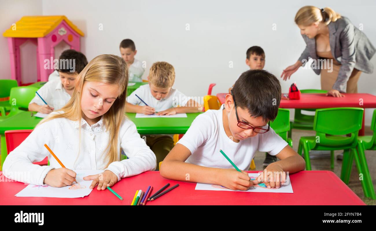 Group of school kids with the pens and notebooks studying in classroom ...