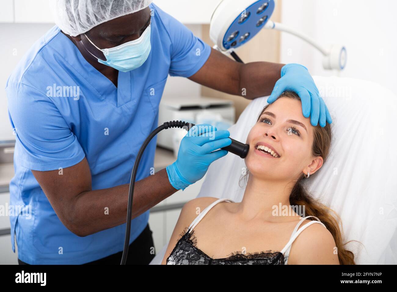 Young woman receiving face ultrasound lifting procedure in clinic of ...