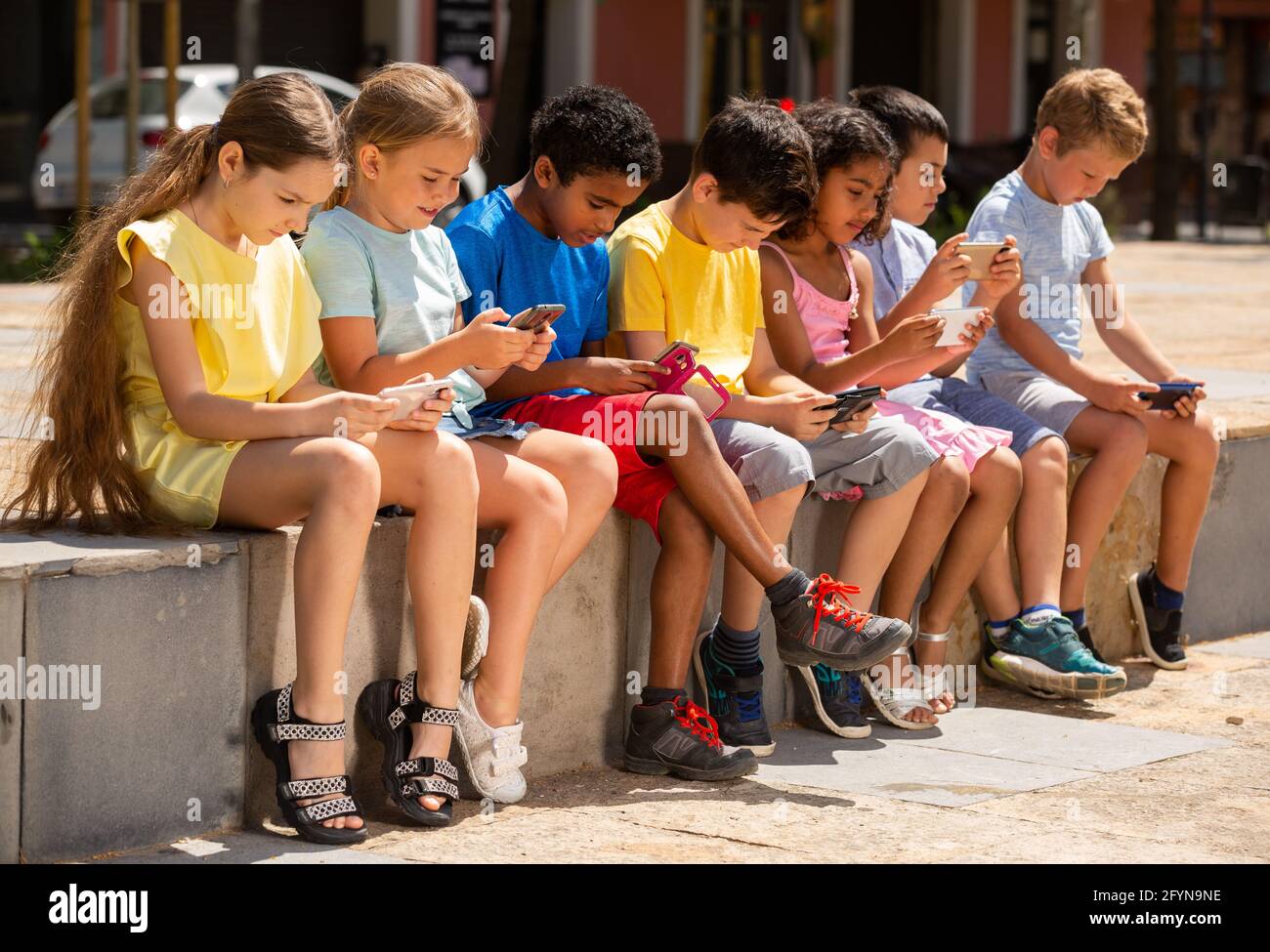 Children chatting on their smartphone, sitting on street parapet Stock ...