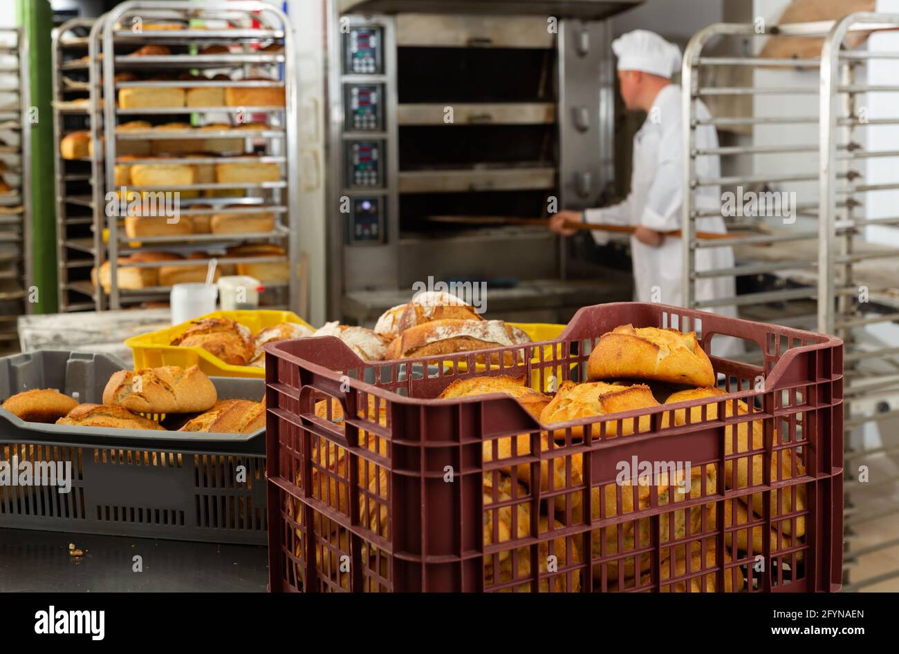 Closeup of freshly baked bread in plastic boxes in private bakery on background with working staff Stock Photo
