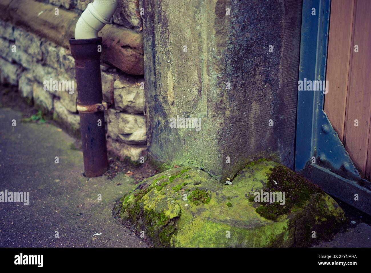 Closeup shot of a sewerage pipe next to an old stone wall and wooden door Stock Photo