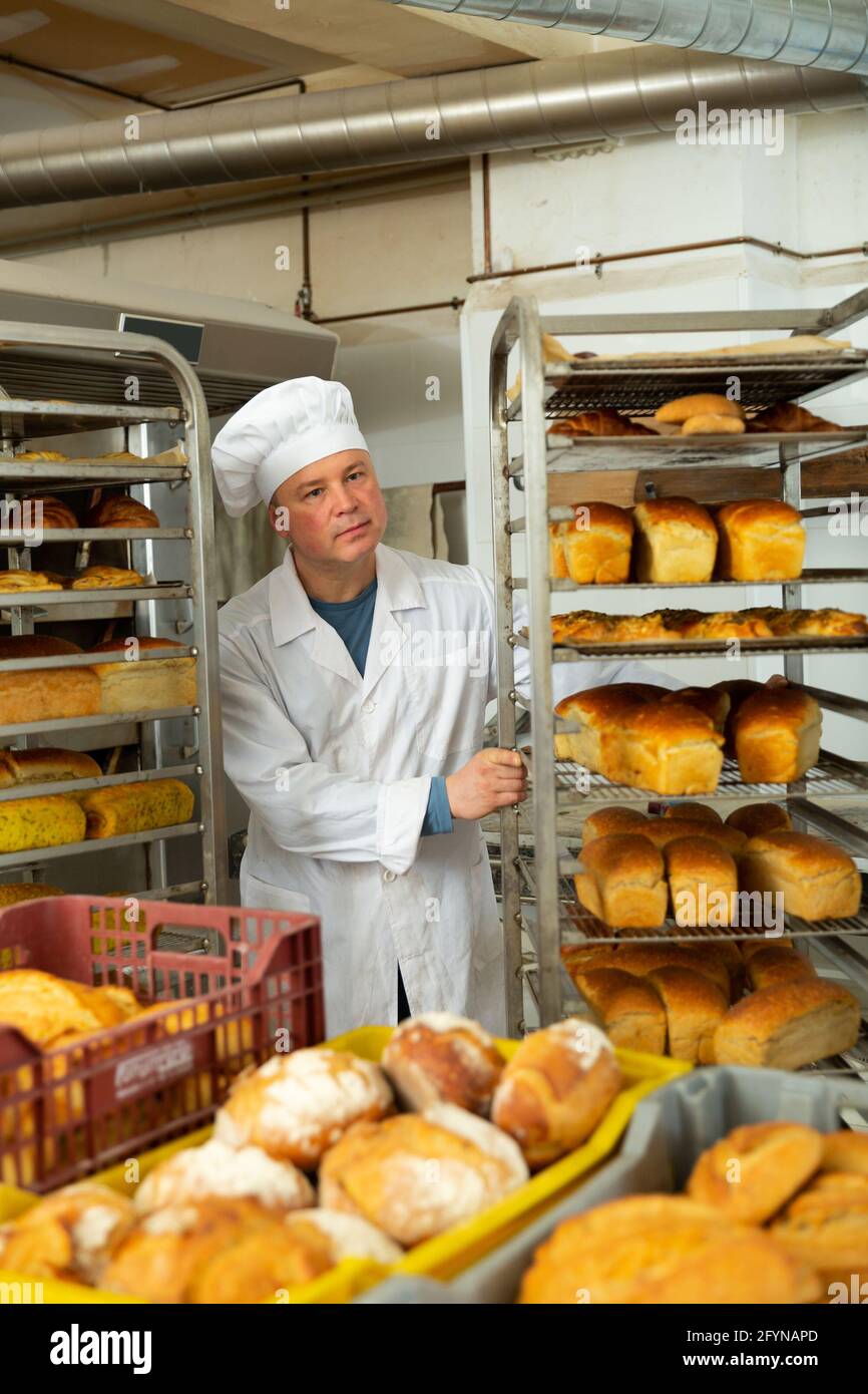 Confident bakery worker pushing rack trolley with freshly baked loaves Stock Photo