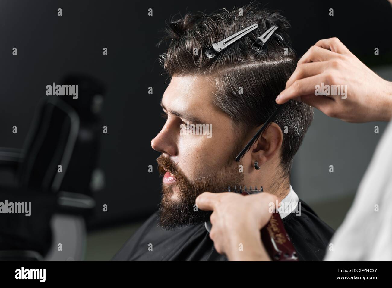 Barber making hairstyle for confident bearded hipster. Advertising for  barbershop and men's beauty salon Stock Photo - Alamy