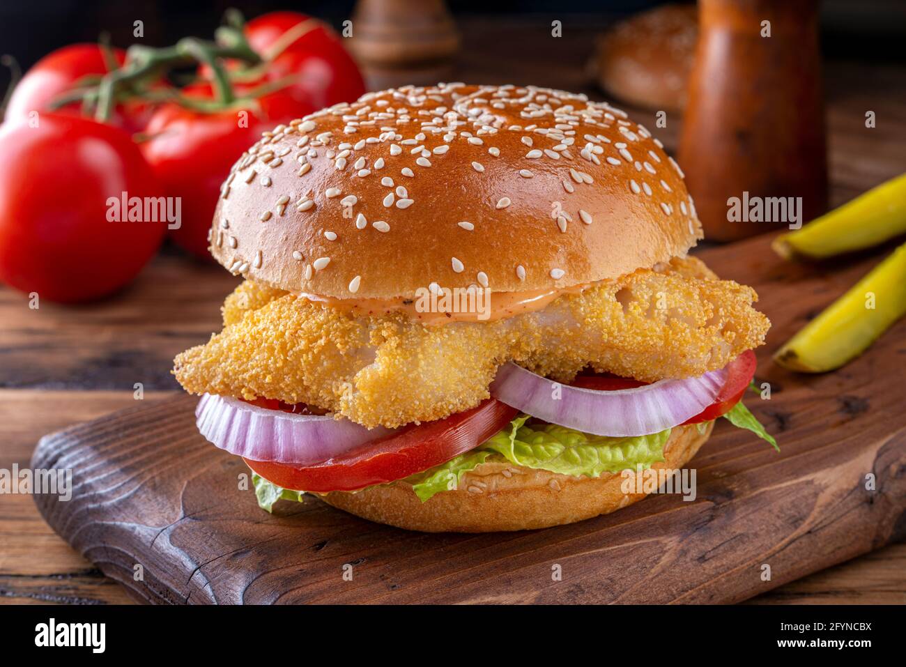 A delicious crispy fried fish sandwich with lettuce, tomato, onion and sriracha mayo. Stock Photo
