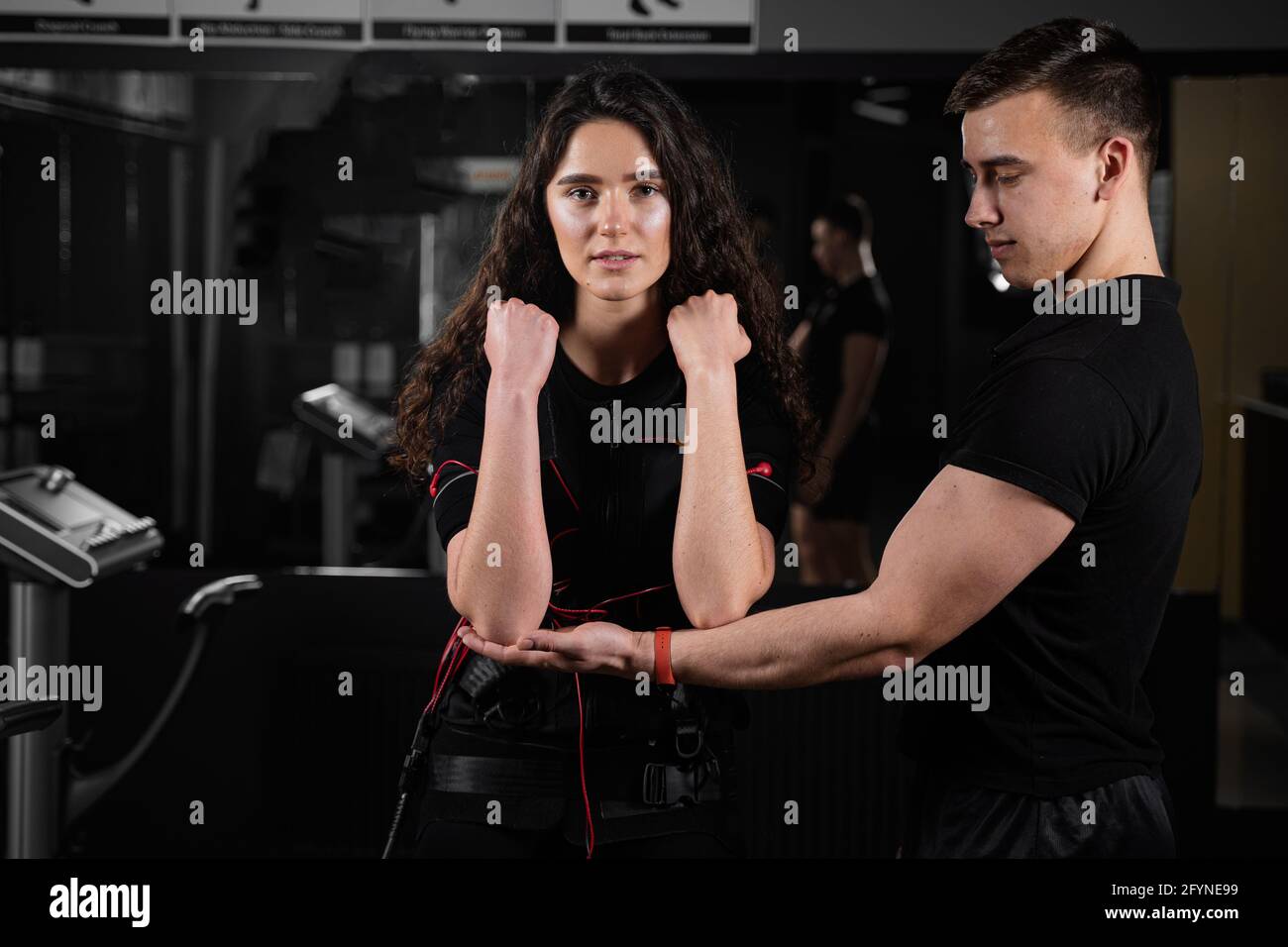 Man trainer trains a girl in an EMS suit in the gym. Electrical ...