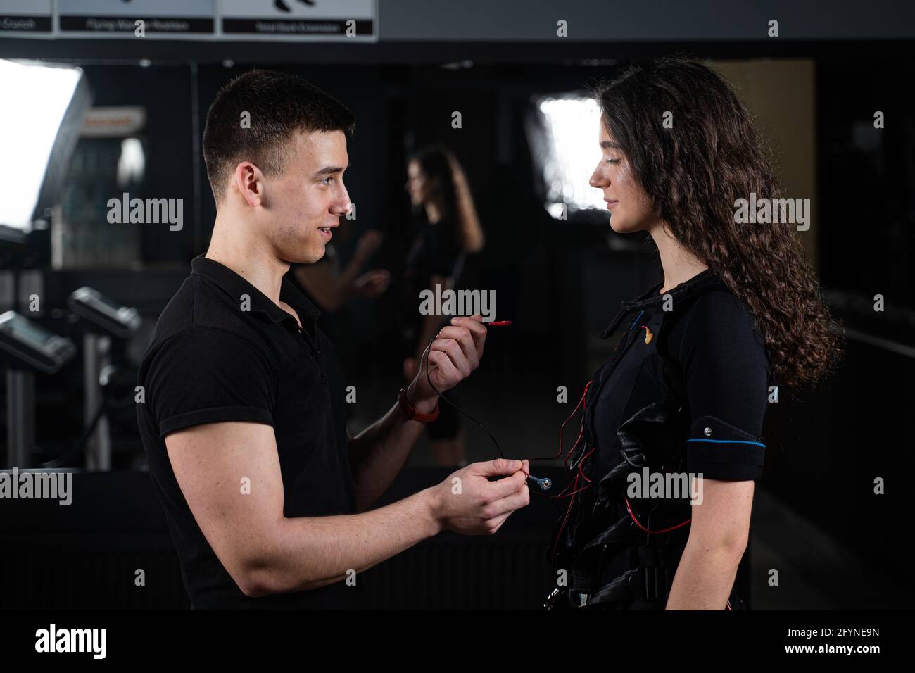 Man trainer trains a girl in an EMS suit in the gym. Electrical ...