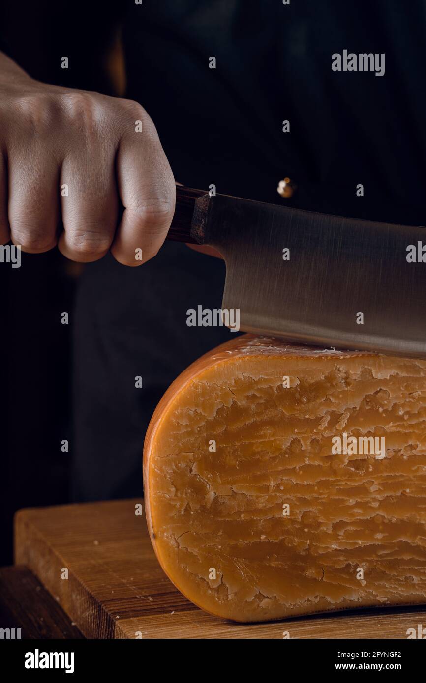 Closeup slicing aged cheese parmesan with crystals using a cheesy