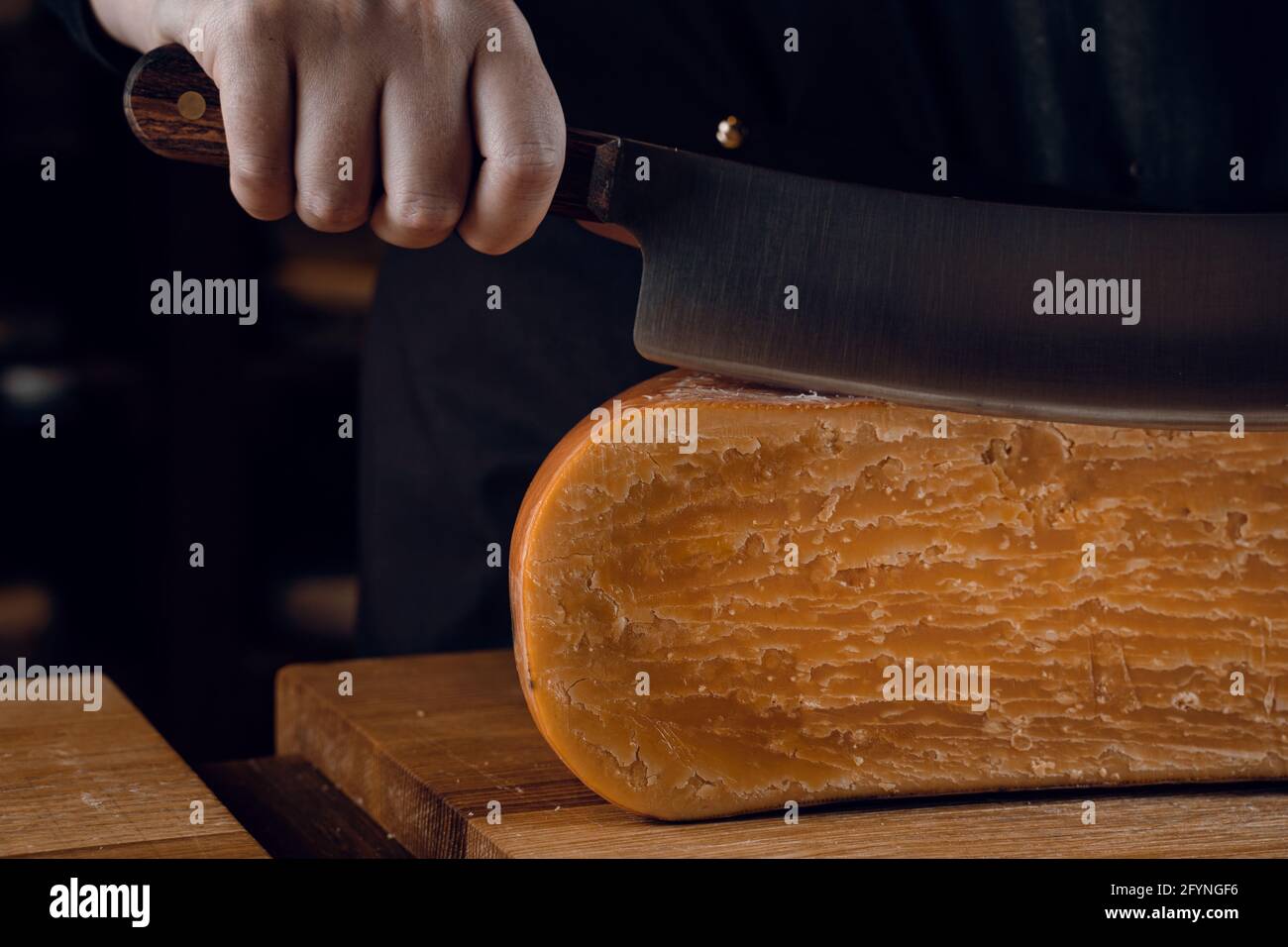 Closeup slicing aged cheese parmesan with crystals using a cheesy
