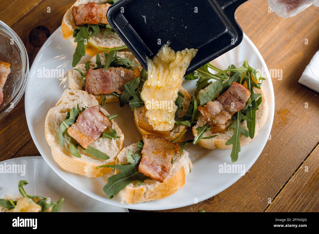Raclette melted cheese for sandwich with fried bacon and arugula ...