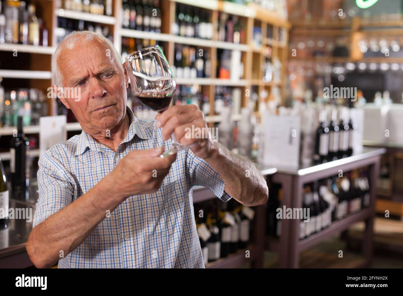 Older man inspecting quality of red wine in wine store in search of perfect wine for solemn