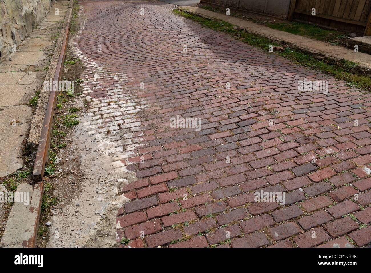 Old red brick street bordered on both sides with crumbling concrete ...